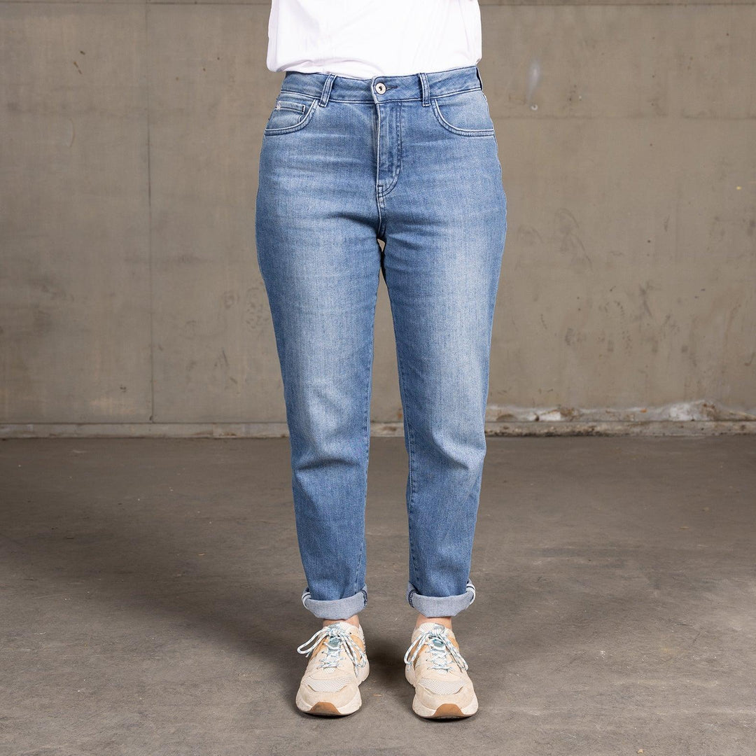 Vooraanzicht van een model dat The Mom jeans van Delft Denim draagt. Deze comfortabele mom jeans is gemaakt van duurzaam denim en heeft een hoge taille, een relaxte pasvorm en omgeslagen zomen voor een casual look