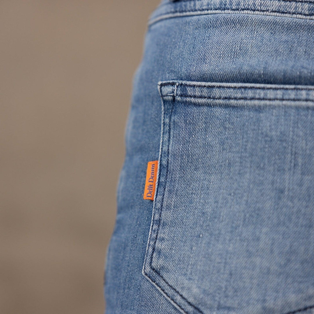 Close-up van de achterzak van The Mom jeans van Delft Denim, met het iconische oranje merklabel. Een duurzame high-waist mom jeans met een relaxte pasvorm en authentieke denim look.