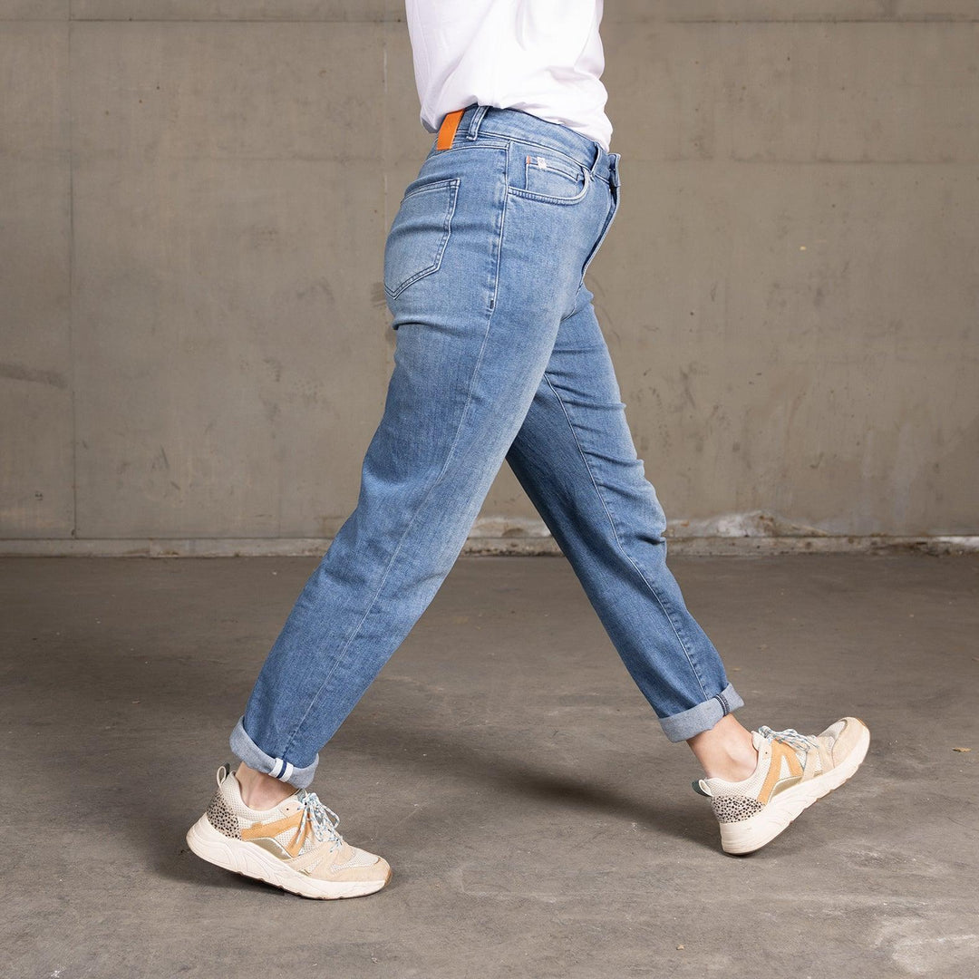 Zijaanzicht van een model dat The Mom jeans van Delft Denim draagt, terwijl ze loopt. Deze high-waist mom jeans heeft een relaxte pasvorm en een lichte denim wassing, perfect voor een casual en comfortabele look.